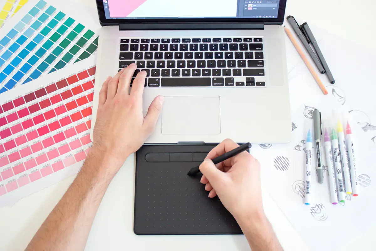 Ontwerper werkt op een laptop met kleurstalen en een tekentablet